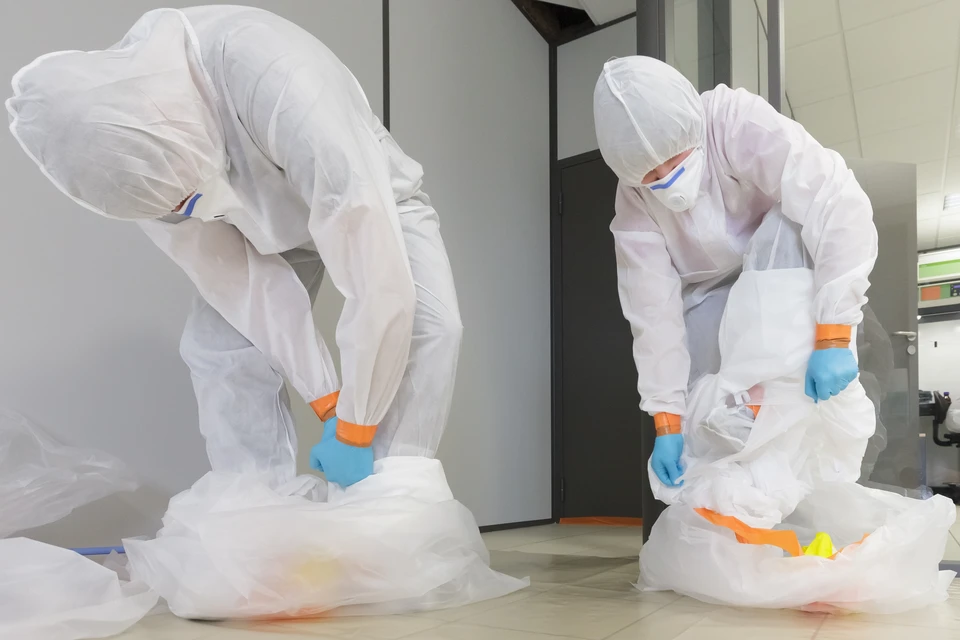 Exploitants en combinaison de fumée de type 5-6 effectuant une procédure de décontamination, après l'incident de l'amiante, décollage prudent de la combinaison de protection dans un grand sac d'élimination