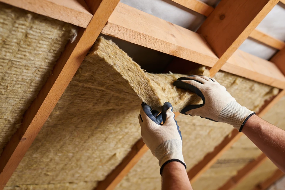Ouvrier en équipement de protection individuelle installant de l'isolation thermique dans les combles d'une habitation