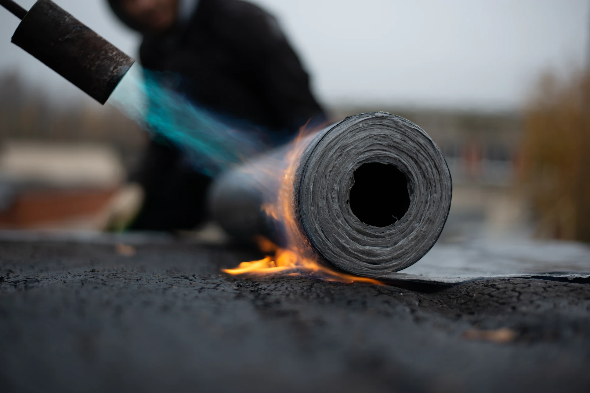 Chantier extérieur de toiture avec ouvrier appliquant un revêtement d'étanchéité au chalumeau sur membrane bitumineuse