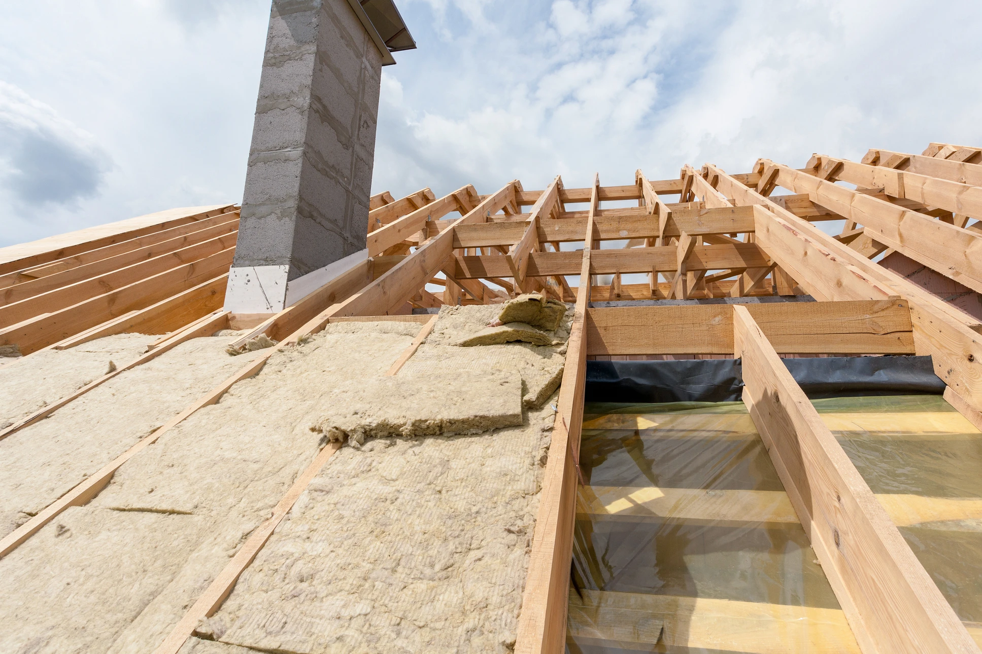 Chantier de construction résidentielle en cours, combles aménageables avec charpente bois apparente et isolation thermique jaune entre chevrons