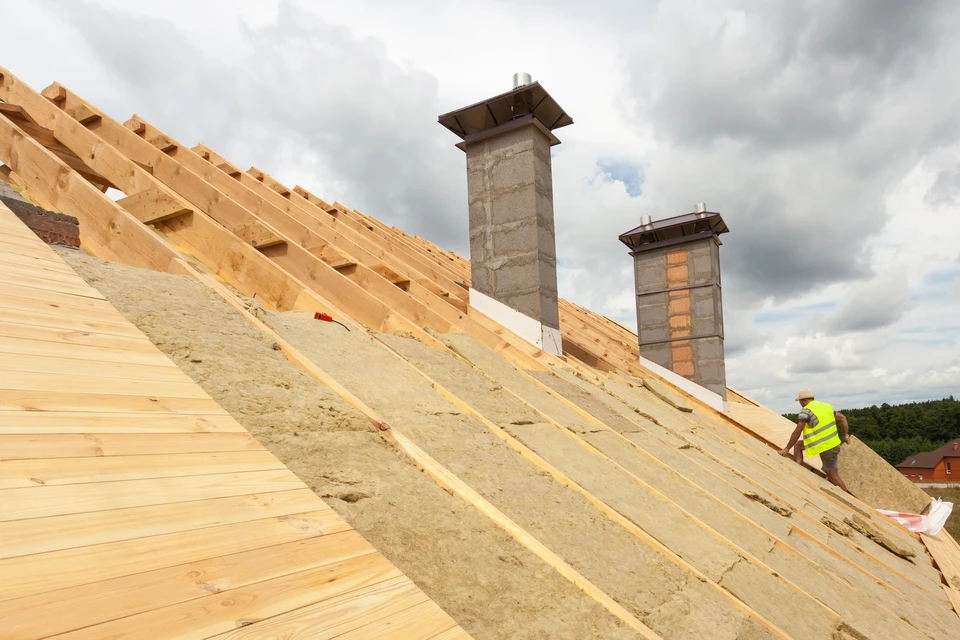 Photographie d'un artisan ou d'une équipe effectuant des travaux de sarking sur une toiture : pose d'isolation thermique en panneaux rigides sur la face externe d'une toiture en pente, avec mise en évidence des couches d'isolation et de protection. La scène montre clairement les matériaux d'isolation thermique, la technique d'application par l'extérieur, et l'amélioration de la performance énergétique du bâtiment. Le contexte doit être professionnel et mettre l'accent sur la protection thermique des combles.